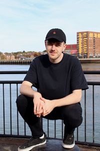 Portrait of young man crouching against railing and sea