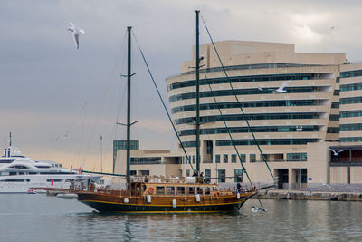 Boats moored at harbor in city against sky