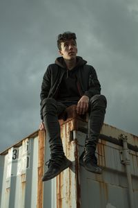 Low angle view of boy looking away while sitting on cargo container