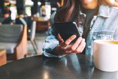 Midsection of woman using phone while sitting on table