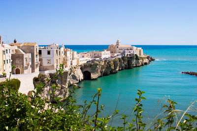 Buildings in sea against clear blue sky