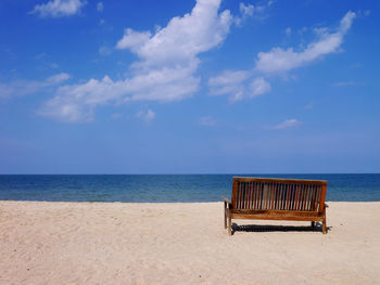 Empty bench on beach against sky