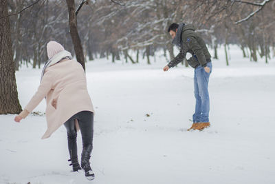 Couple playing on snow filed against bare trees