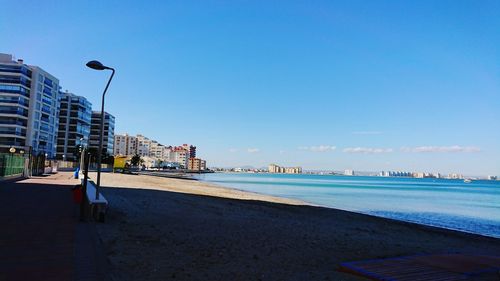Scenic view of beach by buildings against blue sky