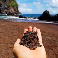 Cropped image of hand holding pebbles at beach