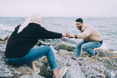 Young woman passing mobile phone to man on rocks at beach