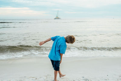 Rear view of playful boy bending at panama city beach against sky