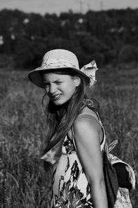 Portrait of young woman wearing hat while standing on grassy field during sunny day