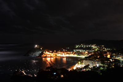 Illuminated cityscape by sea against sky at night