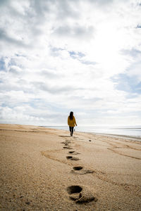 Rear view of woman walking on sand at beach against sky