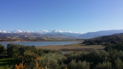 Scenic view of lake and mountains against clear blue sky