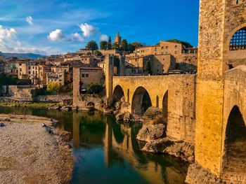 Arch bridge over river by buildings against sky