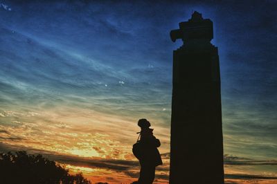 Silhouette woman standing by sculpture against sky during sunset