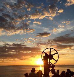 Silhouette people on beach against dramatic sky during sunset