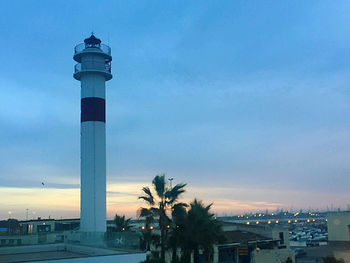 Lighthouse by building against sky during sunset