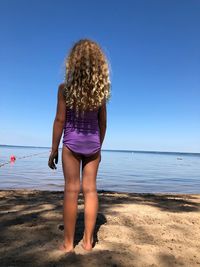 Rear view of girl looking at sea while standing on sand against clear sky