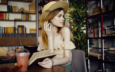 Young woman looking away while sitting on table