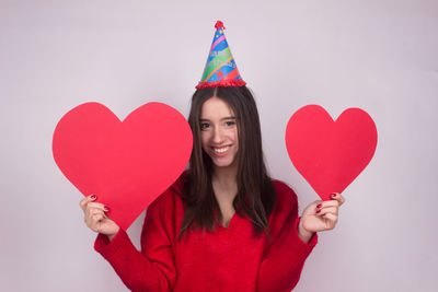 Portrait of woman holding red heart shape over white background