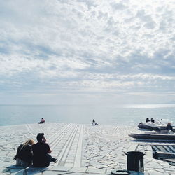 Friends sitting at sea shore against sky