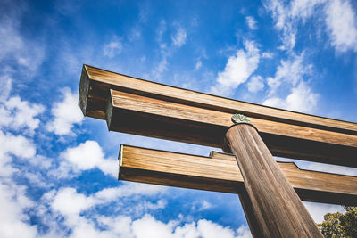 Low angle view of wooden torii against cloudy blue sky