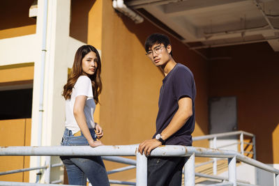 Portrait of young couple standing against railing