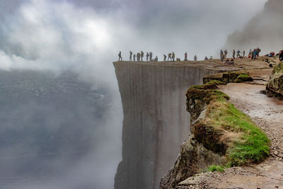 Group of people on rock against cloudy sky