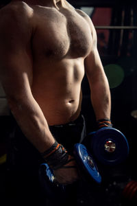 Midsection of shirtless man lifting dumbbells