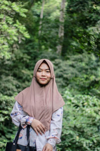 Portrait of smiling woman standing against trees in forest