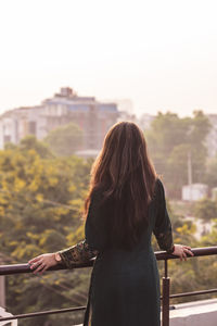 Young girl standing on her balcony during sunset, enjoying the beautiful view of the city.