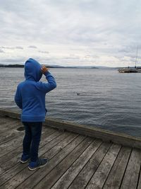 Rear view of boy standing on pier over sea against sky