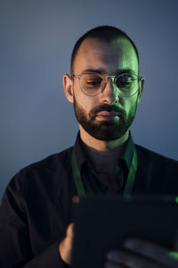 Businessman wearing eyeglasses holding tablet pc in front of gray wall