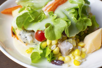 Salad with fruit and fresh vegetable topped with salad dressing in a white dish on wooden table