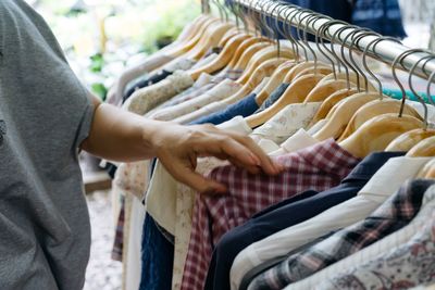 Midsection of woman choosing clothes from rack in store for sale