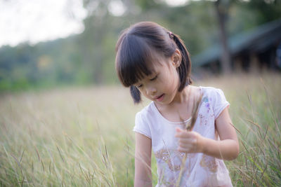 Girl holding reed while standing amidst plant
