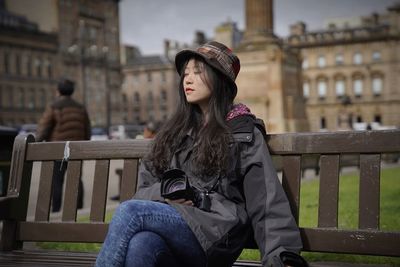 Young woman sitting on railing in city against sky