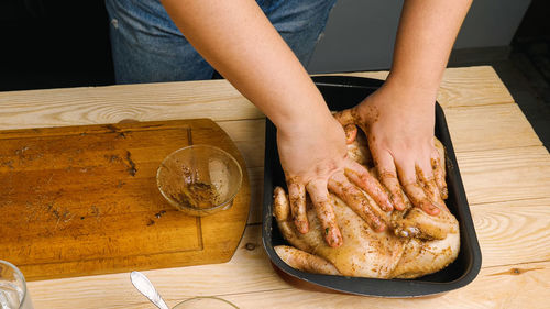 A close-up of a woman's hands smeared with seasoning and spices places a raw chicken in a black