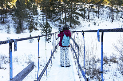 Young woman from behind walking on wooden bridge and holding dog in winter. travel with pet