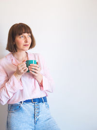 Beautiful young woman drinking water against white background