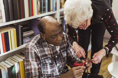 Elderly man knitting while female friend assisting him at retirement home