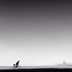 Person riding bicycle on beach against clear sky