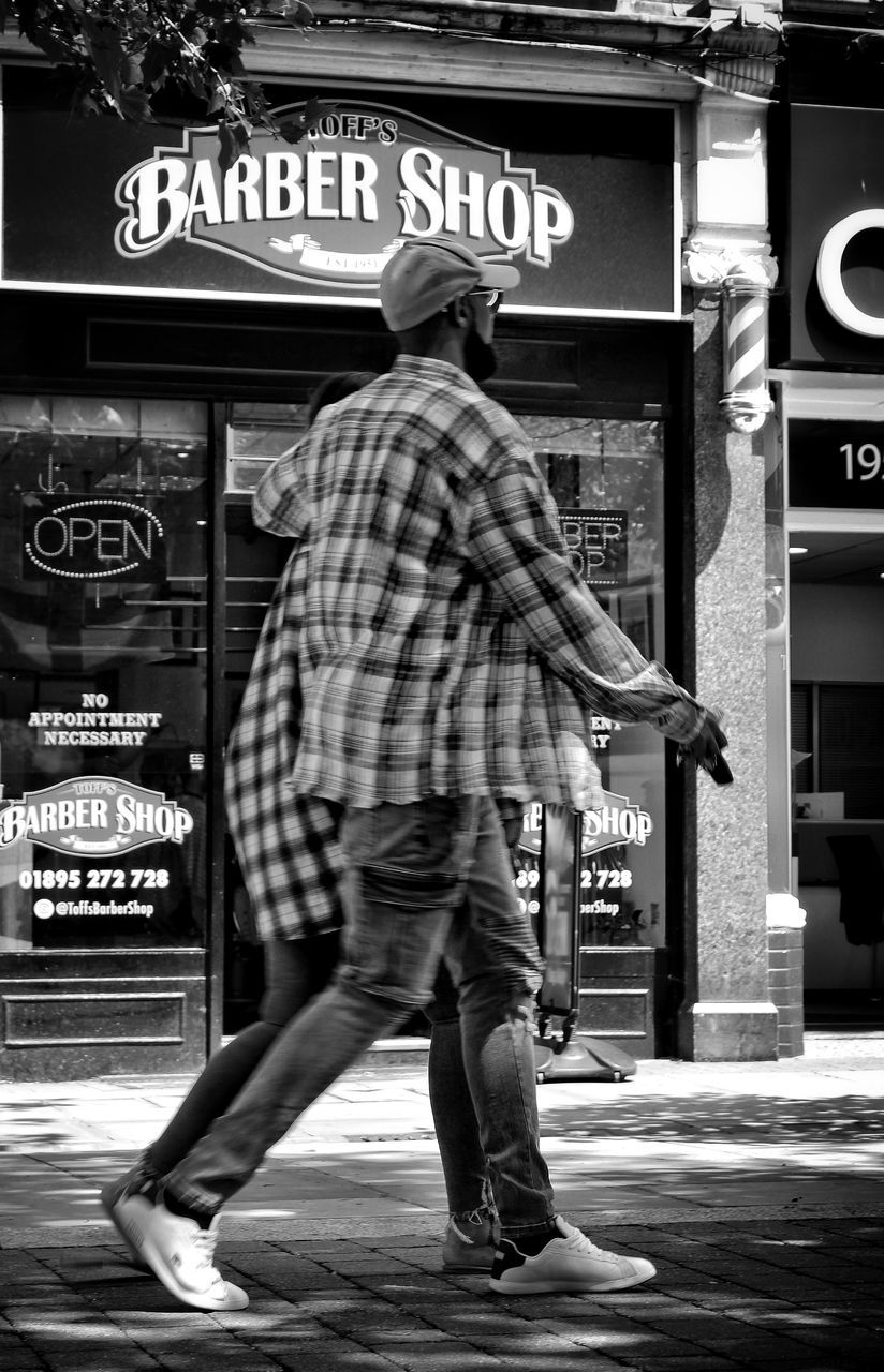 street, road, black, black and white, full length, monochrome, monochrome photography, white, architecture, city, text, one person, men, infrastructure, adult, western script, footwear, casual clothing, built structure, building exterior, lifestyles, footpath, motion, clothing, communication, person, rear view, sign, walking, day, leisure activity, city life, outdoors