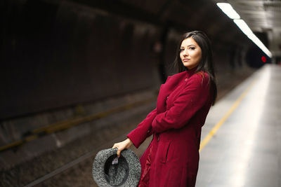 Portrait of young woman standing against red wall