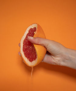 Close-up of hand holding apple against orange background