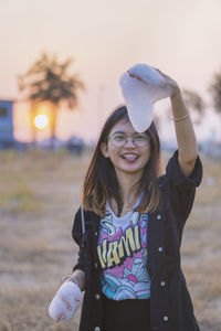 Smiling young woman holding soap sud while standing against sky during sunset