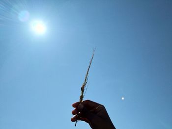 Low angle view of hand holding hands against clear blue sky