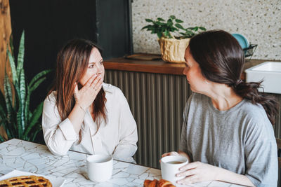 Adult smiling brunette middle aged women sisters friends having breakfast in kitchen at house