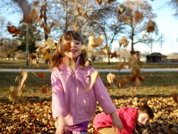 Siblings enjoying with dry leaves at park during autumn