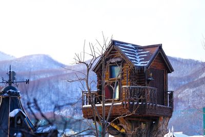 Tree house by mountain against sky during winter