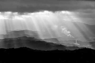 Sunlight streaming through clouds over silhouette mountain