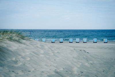 Hooded beach chairs on sea shore against sky